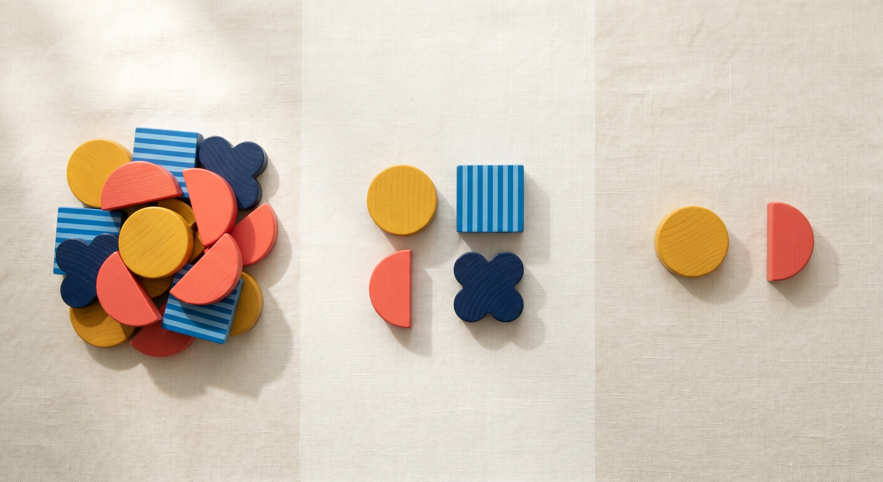 Bauhaus wooden blocks arranged in three clusters on cream linen, from a messy pile to a neat group to a minimal pair