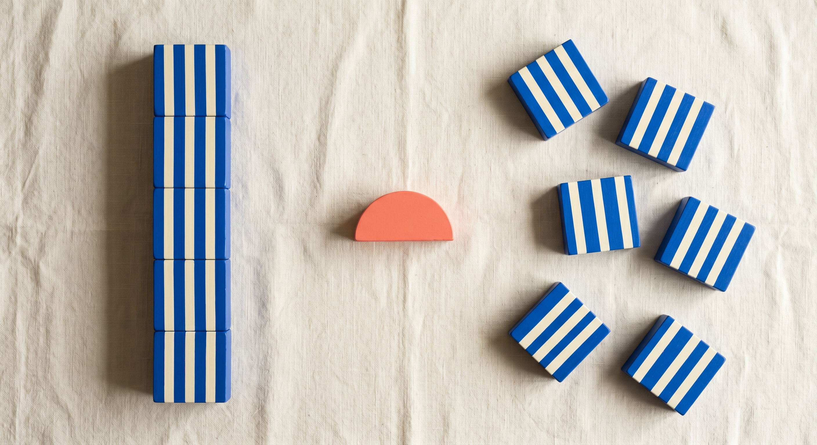 Neat vertical stack of blue striped squares on the left with the same squares scattered loosely on the right on cream linen