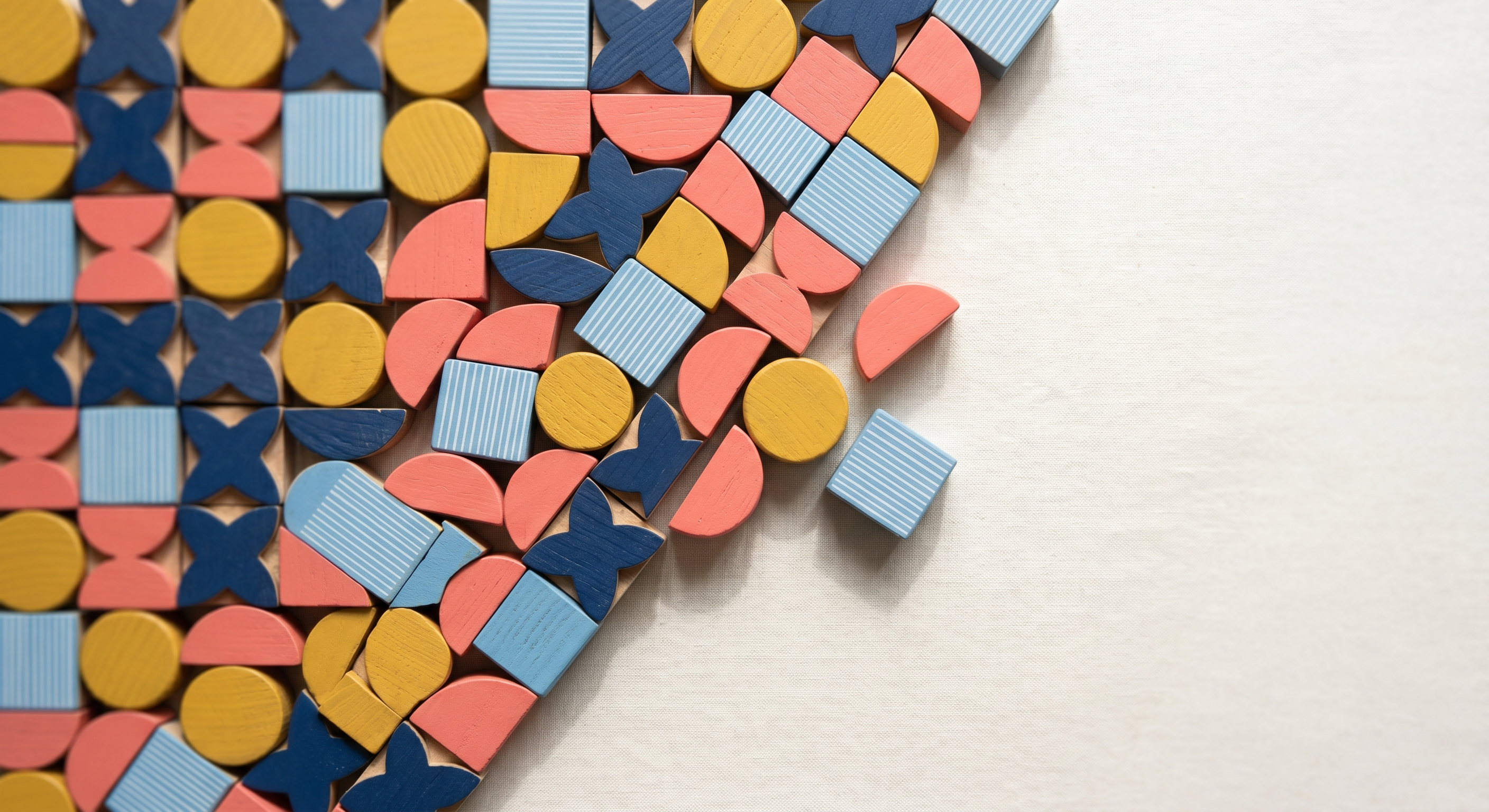 Packed grid of Bauhaus wooden blocks with a diagonal cut to bare cream linen on the right