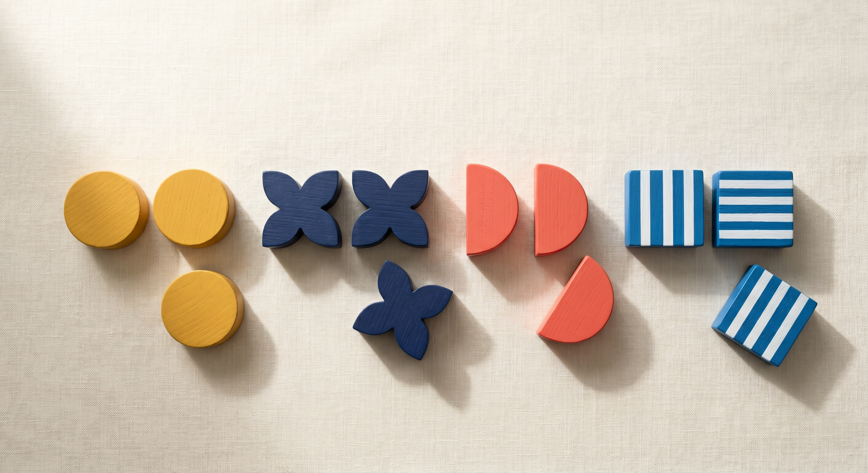 Pairs of identical Bauhaus wooden blocks side by side with one from each pair being separated on cream linen