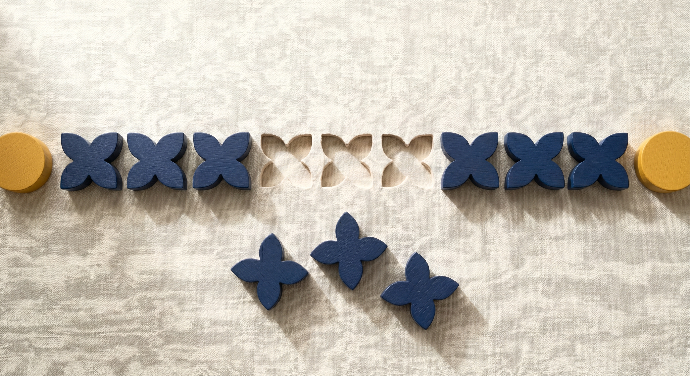 Row of navy wooden four-petal shapes with three removed and clustered below the line on cream linen